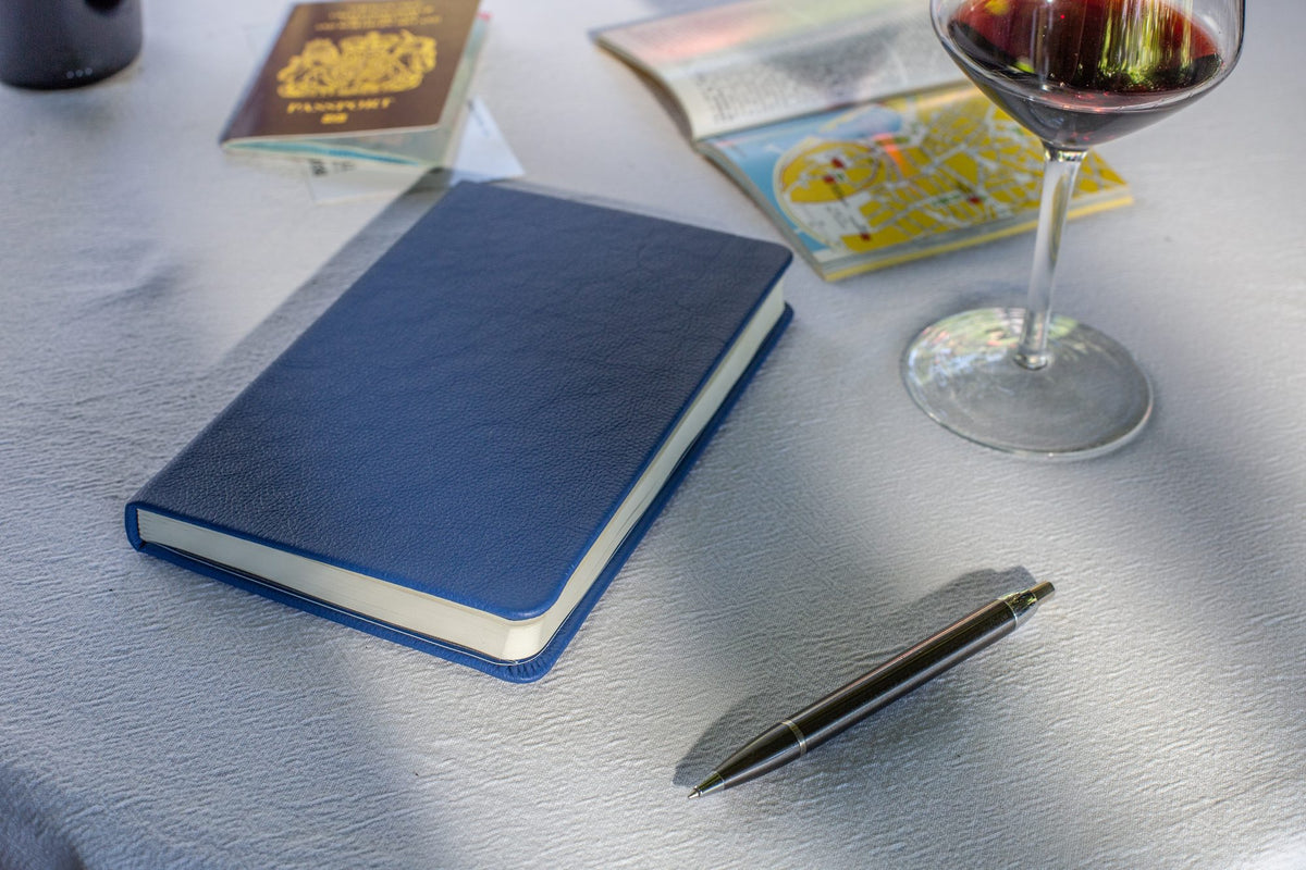 A Pacific Blue Inspire notebook on a café table beside a glass of wine