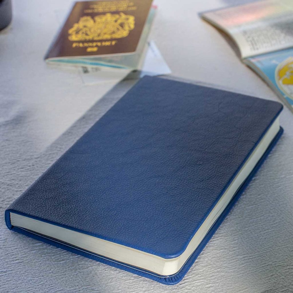 Blue travel notebook on a table with a passport and map visible