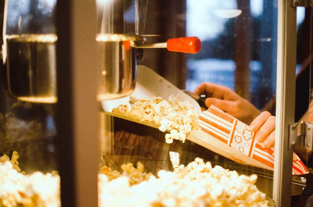 Worked scooping popcorn into a red and white striped popcorn box from a movie theater popcorn machine