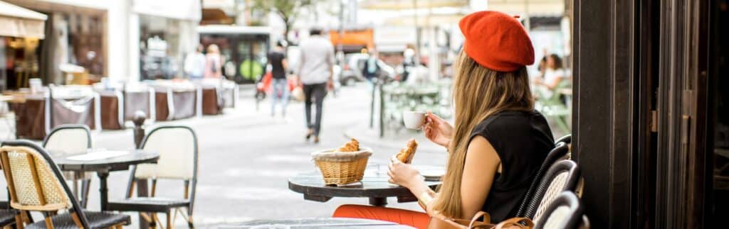 Girl with a reddish orange beret sitting at a table on the street